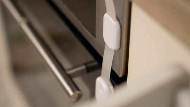 Kindersicherung für Schrank- oder Ofentüren mit weißem Sicherheitsriegel befestigt
